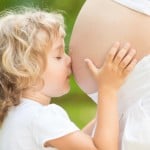 Barn kysser mave på gravid kvinde