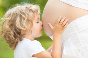Barn kysser mave på gravid kvinde