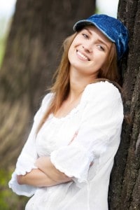 Pige med denim cap læner sig op ad træ